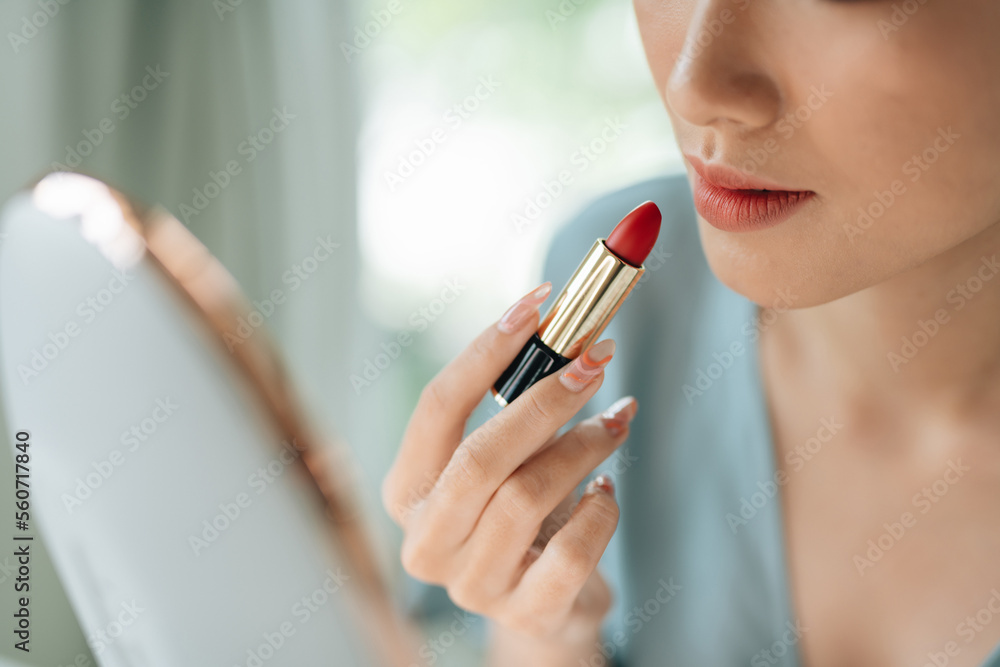 A beautiful elegant woman applying lipstick using a mirror A beautiful elegant woman applying lipstick using a mirror