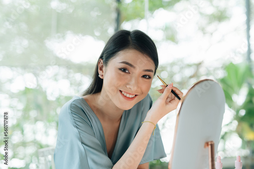 A young woman looks into a round mirror and draws her eyebrows photo