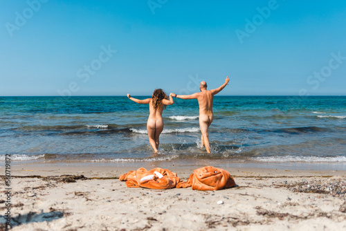Naked couple running for a swim together clothes left on the shore photo