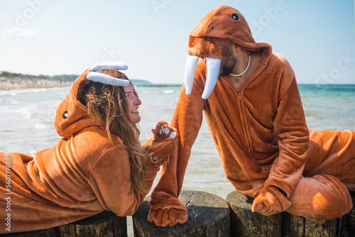Couple dressed as walruses chilling on a wooden breakwater talking