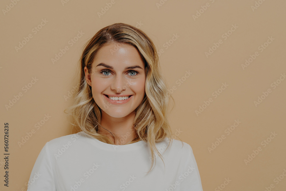 Studio shot of young pretty female with wavy hair in white tshirt looking with satisfaction at camera Studio shot of young pretty female with wavy hair in white tshirt looking with satisfaction at camera