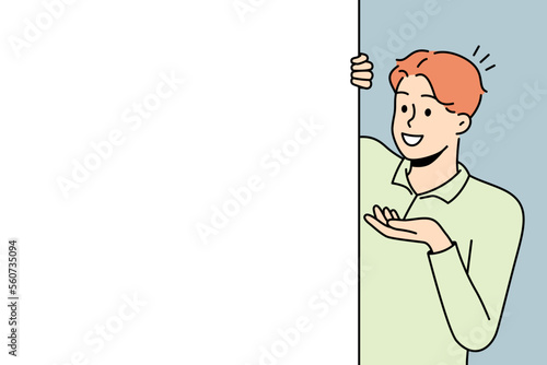 Smiling young man look behind mockup white poster show good deal or offer. Happy male recommend promotion on empty placard. Copy space. Vector illustration. 