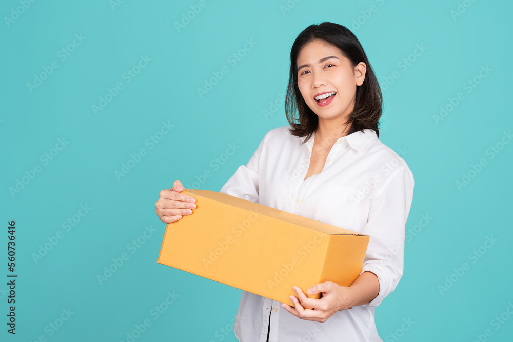 Happy Asian woman smiling in white casual dress standing smiling and looking at camera. She is holding package parcel box isolated on light green background. Happy Asian woman smiling in white casual dress standing smiling and looking at camera. She is holding package parcel box isolated on light green background.