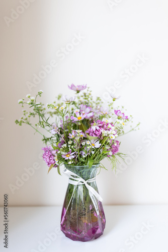 Colorful bouquet of wild flowers in a vase on table on beige background 