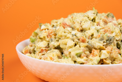 Olivier russian salad in a plate on an orange background close-up.