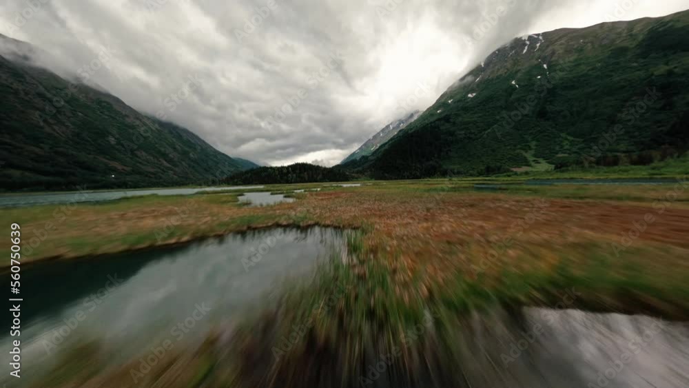 FPV drone flying over Alaskan lake with storm clouds and lush green mountain range in the background