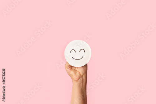 Mano sosteniendo un corte de papel de cara de sonrisa feliz sobre un fondo rosa pastel liso y aislado. Vista de frente y de cerca. Copy space