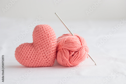 Crocheted amigurumi pastel pink heart with crochet hook and skein of yarn on a white background. Valentine's day banner with copy space, gift with love symbol, handcraft for health concept