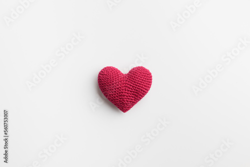 Crocheted amigurumi pink red heart on a white natural solid background, top view with empty space. Valentine's day banner, postcard, love symbol, handicraft for health concept
