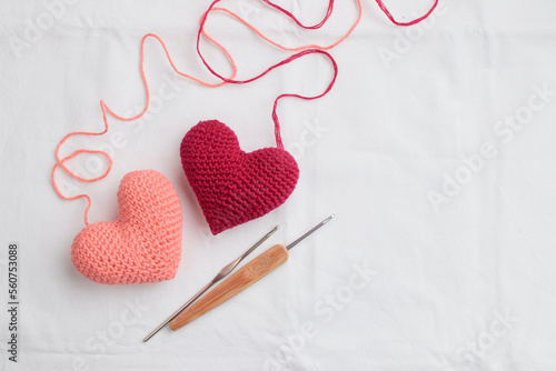 Two crocheted amigurumi pink hearts with a crochet hooks on a white background. Valentine's banner top view