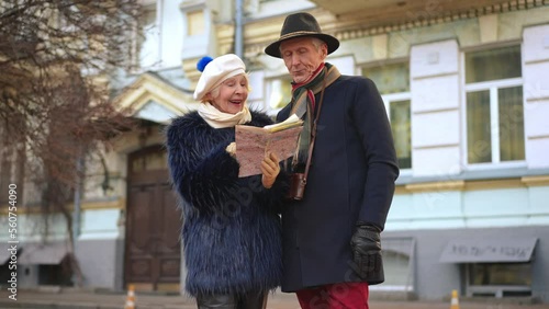 Senior woman talking choosing direction standing with paper map outdoors as man rolling eyes sighing. Portrait of curios Caucasian wife and unsatisfied husband travelling in Europe