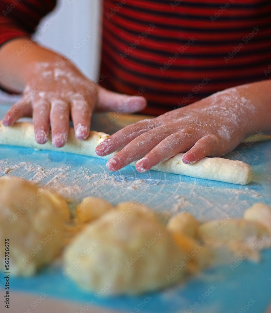 The child prepares lazy dumplings in the kitchen. Children's cooking. Board for rolling dough, flour, dough, dumplings on the table.