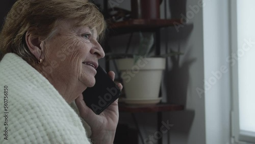 An elderly woman is talking on the phone and laughing