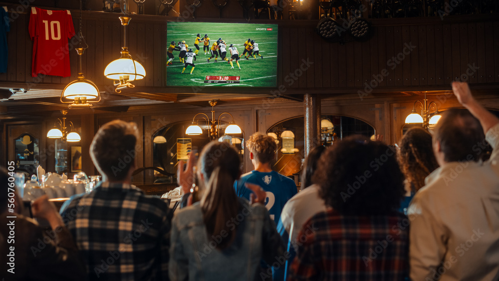 Group of American Football Fans Watching a Live Match Broadcast in a Sports Pub on TV. People Cheering, Supporting Their Team. Crowd Goes Ecstatic When Team Scores a Goal and Wins the Championship. - obrazy, fototapety, plakaty 