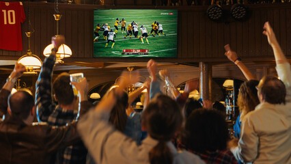 Group of American Football Fans Watching a Live Match Broadcast in a Sports Pub on TV. People Cheering, Supporting Their Team. Crowd Goes Ecstatic When Team Scores a Goal and Wins the Championship.