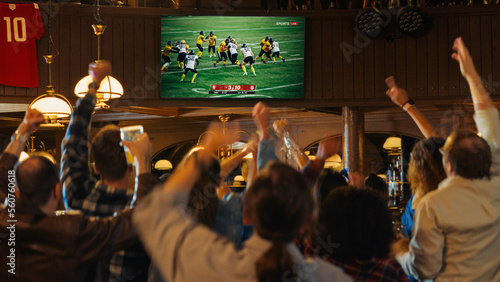 Group of American Football Fans Watching a Live Match Broadcast in a Sports Pub on TV. People Cheering, Supporting Their Team. Crowd Goes Ecstatic When Team Scores a Goal and Wins the Championship.