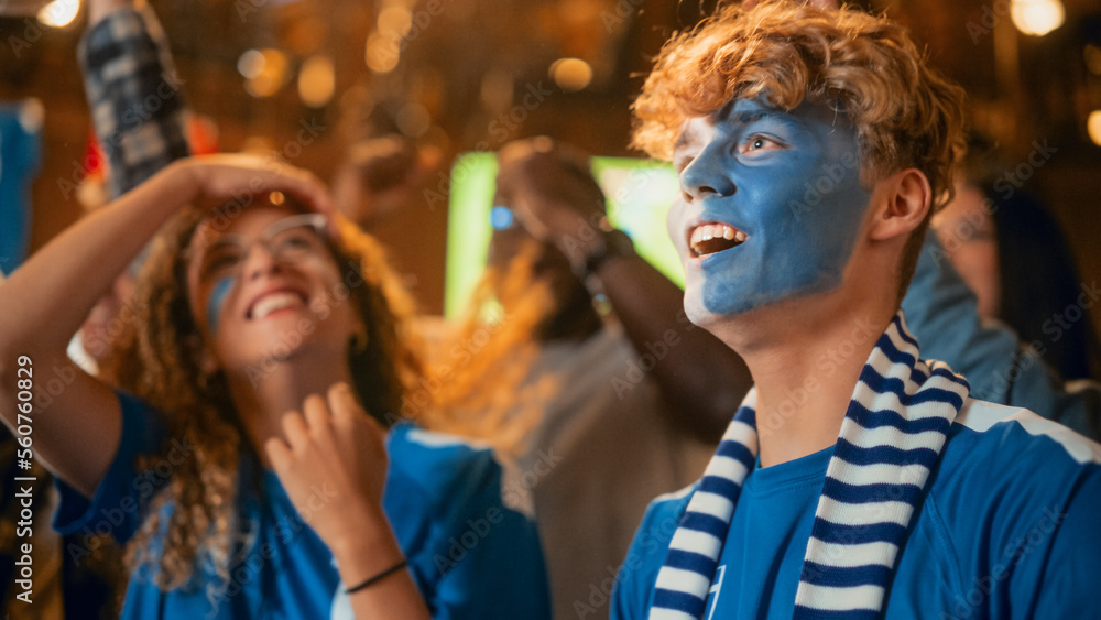 Fototapeta premium Group of Soccer Fans with Painted Faces Cheering, Screaming, Raising Hands and Jumping During a Football Game Live Broadcast in a Sports Pub. Player Scores a Goal and Friends Celebrate. Slow Motion.