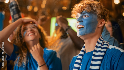 Group of Soccer Fans with Painted Faces Cheering, Screaming, Raising Hands and Jumping During a Football Game Live Broadcast in a Sports Pub. Player Scores a Goal and Friends Celebrate. Slow Motion.