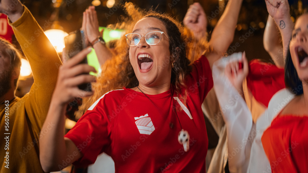 Fototapeta premium Excited Female Holding a Smartphone, Nervous About the Sports Bet She Put on a Her Favorite Soccer Team. Ecstatic Emotions When Football Team Scores a Goal and She Wins a High Stakes Lottery Prize.