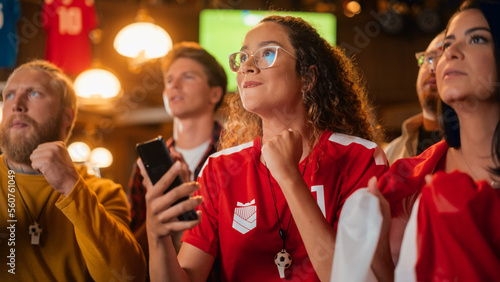 Portrait of an Anxious Multiethnic Female in Red Jersey Holding a Smartphone, Nervous About the Sports Bet on Her Favorite Soccer Team. Happy Victorious Emotions When Football Team Scores a Goal.