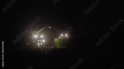 Harvesting corn for silage by a farmer. At night, a combine harvester and a tractor harvest corn in the countryside. Distant plan. photo