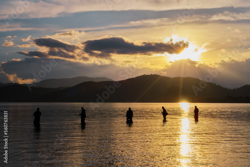 Silhouettes of fishermen against the background of the setting sun  clouds and silhouettes of mountains  selective focus  idea for a background or wallpaper  beautiful natural landscape