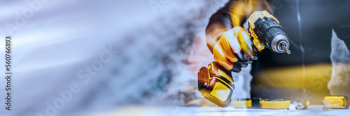 Obraz na plátně Man worker holds an electric screwdriver in his hands close-up against the background of a construction tool and a concrete wall