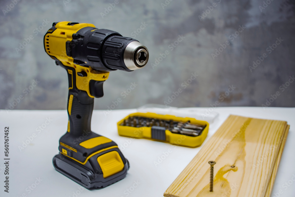 Electric cordless screwdriver on the battery on the table with a self-tapping screw in the board. Electric cordless screwdriver on the battery on the table with a self-tapping screw in the board.