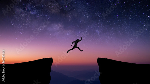Silhouette of young traveler and backpacker jumping on cliff at night with the star and milky way over the sky. He enjoyed traveling and was successful when he reached the summit.