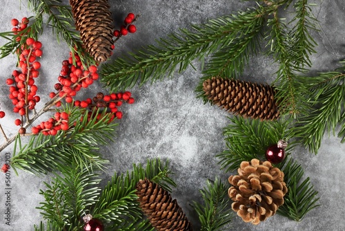 Moderne weihnachtliche Dekoration mit Tannenzweigen, Tannenzapfen, roten Beeren und Kristbaumkugeln auf Beton Hintergrund