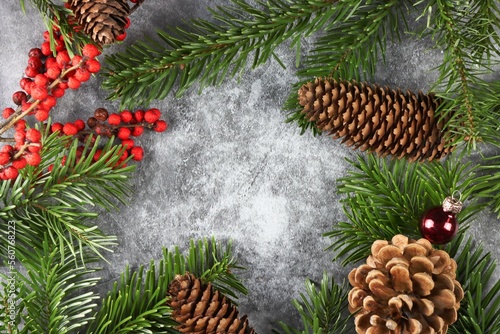 Moderne weihnachtliche Dekoration mit Tannenzweigen, Tannenzapfen, roten Beeren und Kristbaumkugeln auf Beton Hintergrund