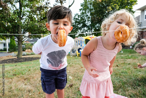 Siblings eating donuts hanging on rope in yard during celebration photo