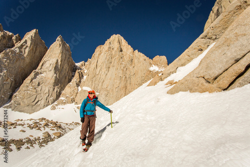 MT. WHITNEY, MOUNTAINEER'S ROUTE, LONE PINE, CA, USA. A 30 year-old woman in mountaineering clothes smiles as she descends a steep snow field with jagged granite peaks rising behin photo