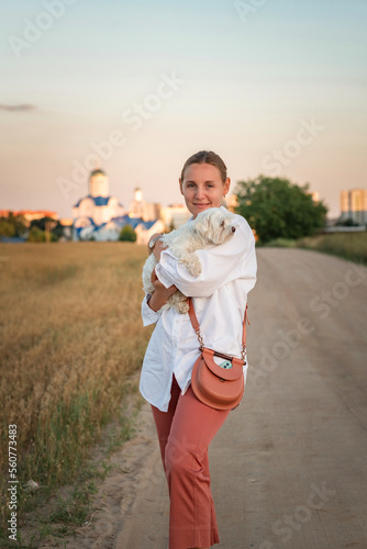 Portrait of a young beautiful blonde with a Maltese in her arms on a summer day outdoors.