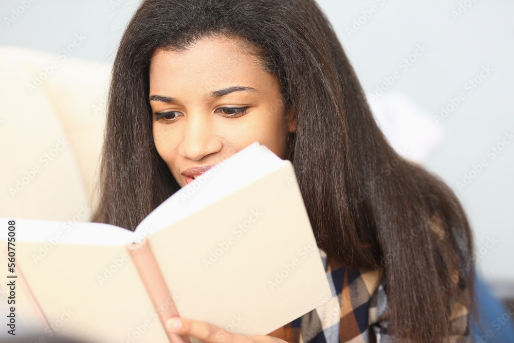 Black woman reads magazine and catalog on sofa in her living room Black woman reads magazine and catalog on sofa in her living room