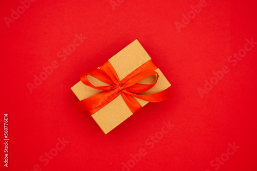 Kraft paper gift box with ribbon bow from above, red background.