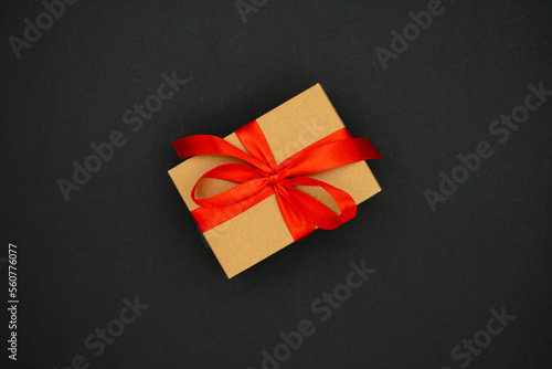 Present box from brown paper with red ribbon bow, isolated on black background. Celebration concept