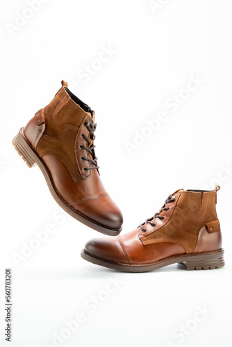 Men pair of boots casual style in camel colour over a white background. Side view  one foot suspended  in the air. Copy space for ad  design  text.