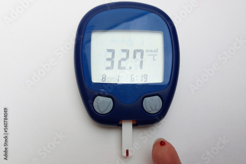 A blood glucose meter with a high blood sugar reading lies on a wooden table. Blood sugar measurements. The concept of diabetes. Hypoglycemia. Copy space. photo