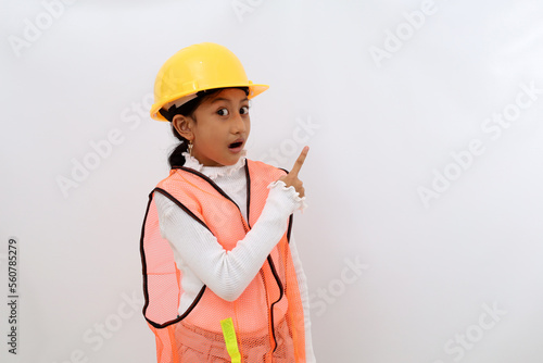 Amazed Asian little girl in the construction helmet as an engineer standing while pointing sideways. Isolated on white with copyspace © SetianingDyah