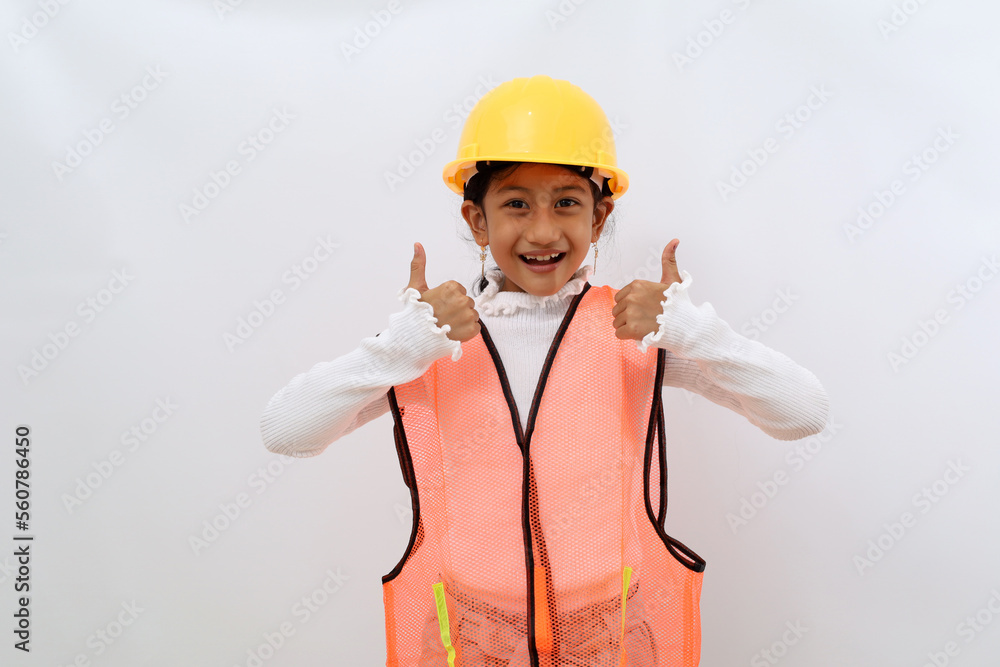 Cheerful Asian little girl in the construction helmet as an engineer standing while showing thumbs up. Isolated on white with copyspace