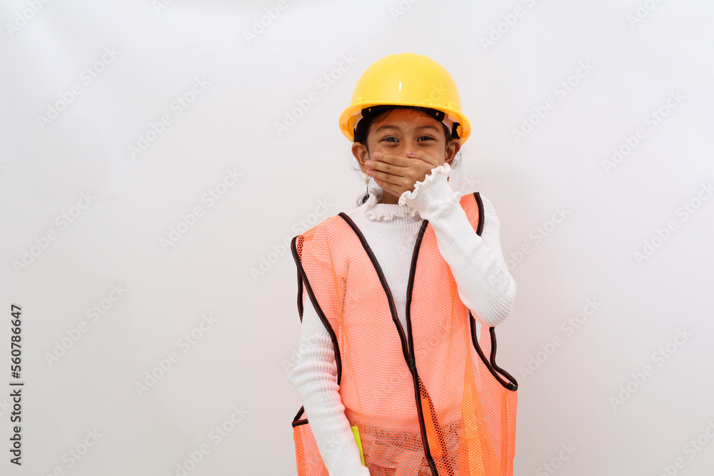 Adorable Asian little girl in the construction helmet as an engineer smiling while covering her mouth. Isolated on white with copyspace