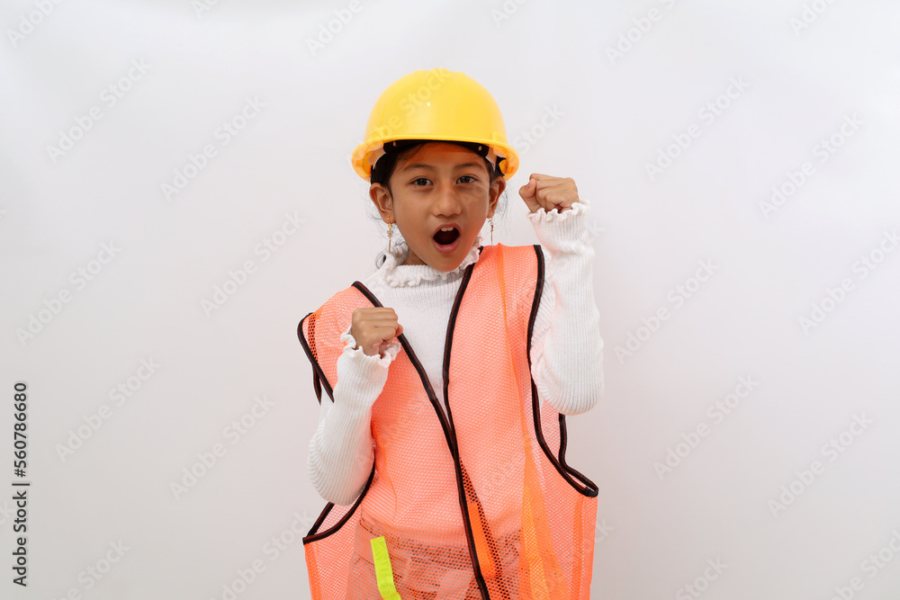 Successful Asian little girl in the construction helmet as an engineer standing with clenched or fist hands. Isolated on white