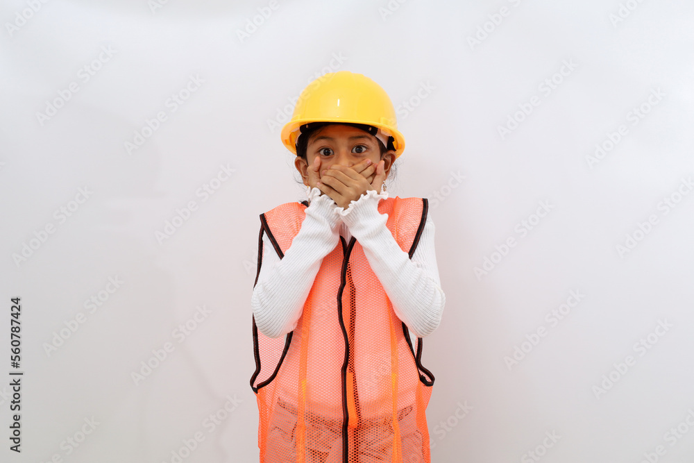 Shocked Asian little girl in the construction helmet as an engineer standing while covering her mouth. Isolated on white Shocked Asian little girl in the construction helmet as an engineer standing while covering her mouth. Isolated on white