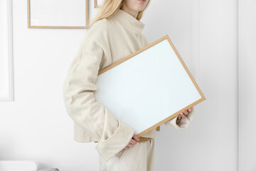 Woman with big blank frame near light wall