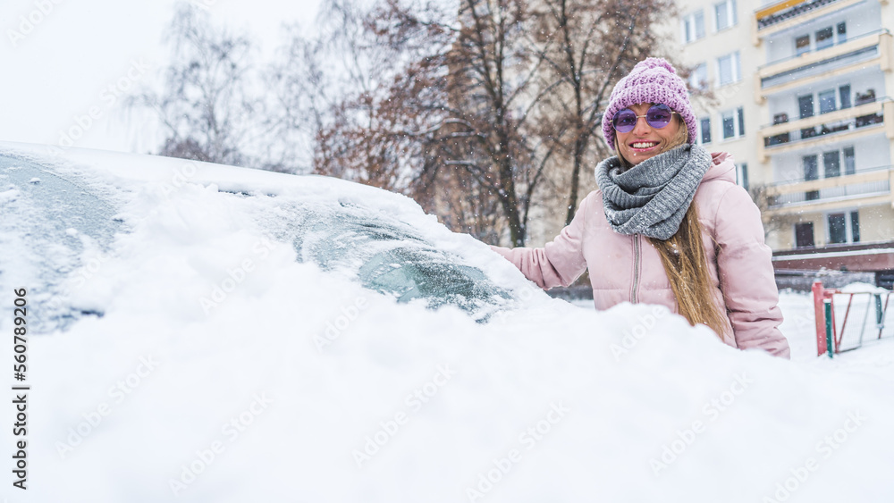 Portrait of a young woman near the car covered in snow. Winter clothing in pink. High quality photo