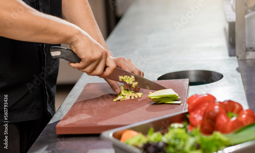 Professional chef in uniform preparing fresh vegetables on cutting board in restaurant kitchen. Culinary concept