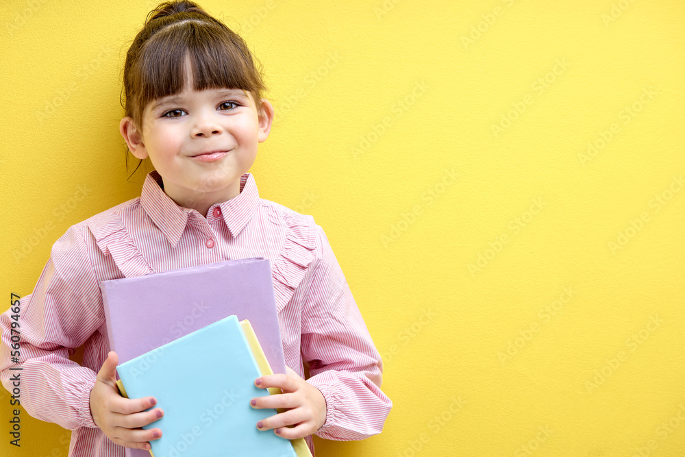 Diligent child girl holding books in hands and looking at camera isolated over yellow background. Little kid love education, studying Diligent child girl holding books in hands and looking at camera isolated over yellow background. Little kid love education, studying