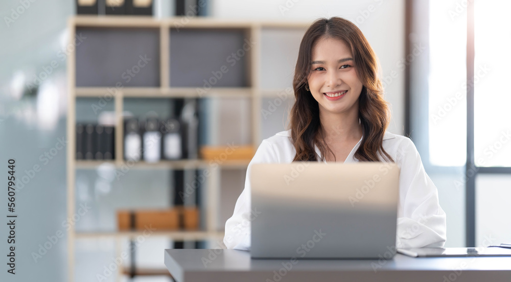 Charming Asian woman working at the office using a laptop Looking at the camera. Charming Asian woman working at the office using a laptop Looking at the camera.