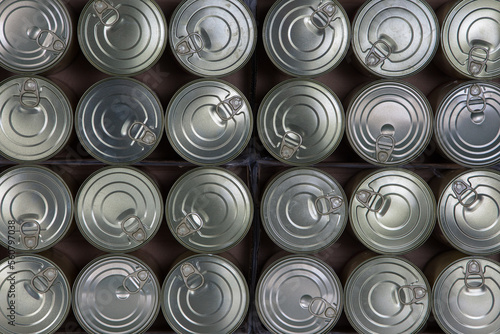 Food behind sheet metal. Lined up tin cans with pull-off lids viewed from above.